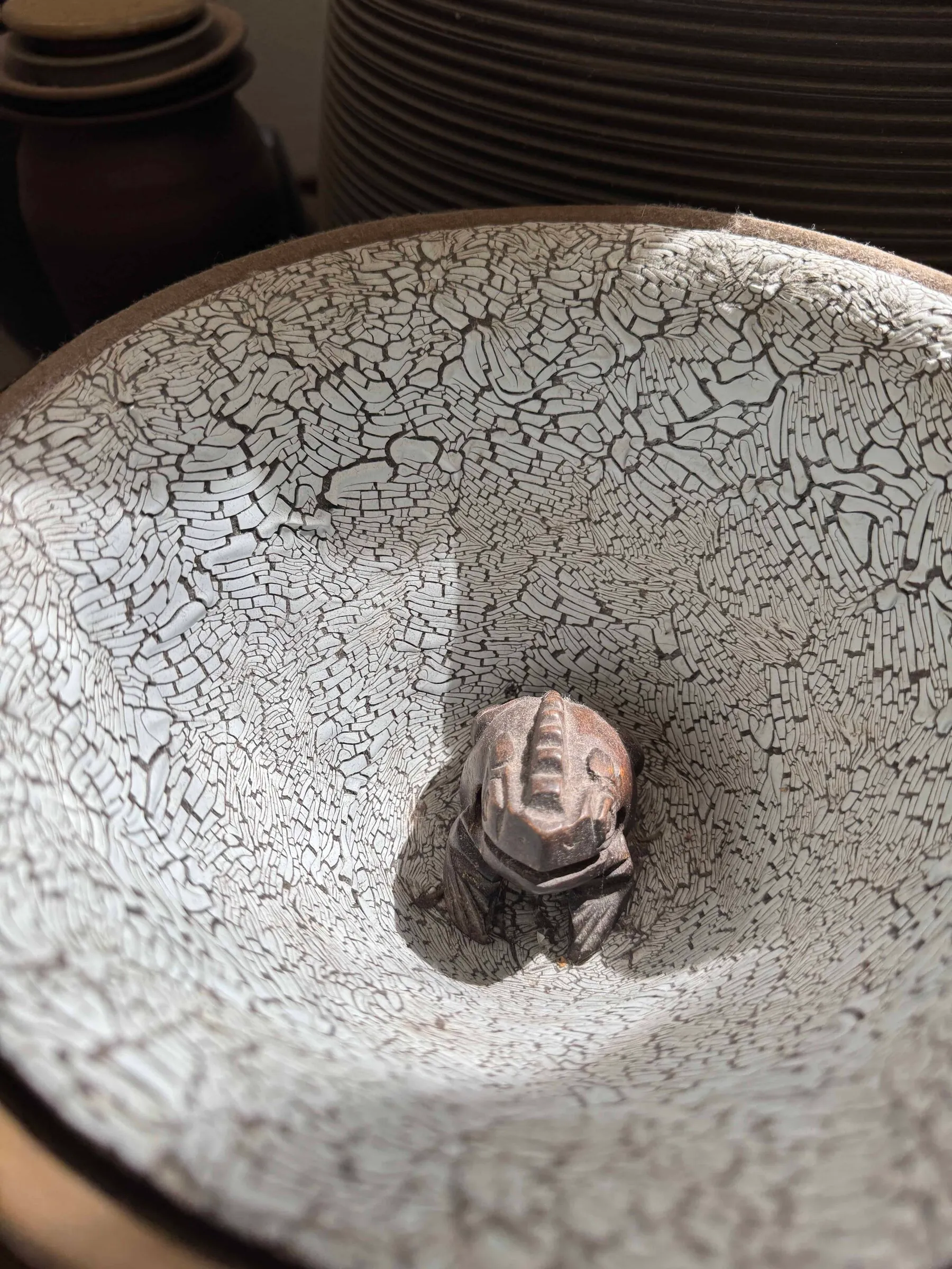 A wide white crackle-glazed bowl with a small clay figure sitting in its centre