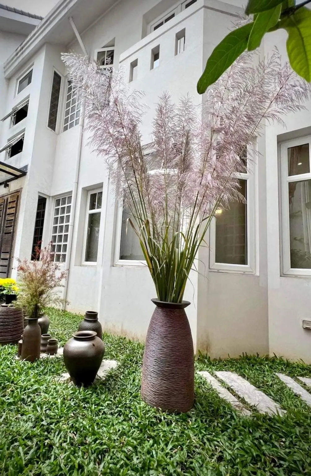 A tall dark vase with pink pampas grass standing in a garden