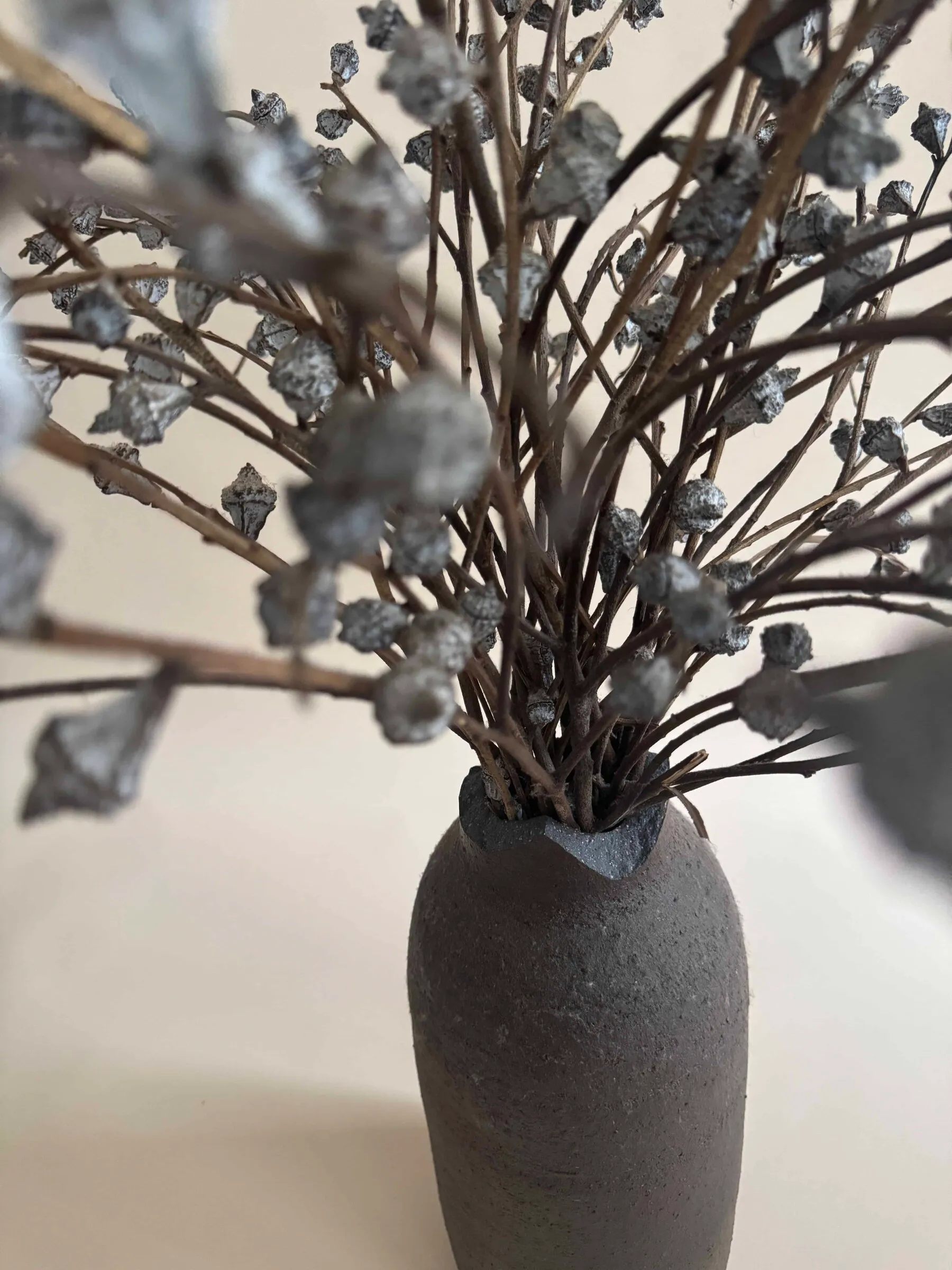 A matte grey vase holding a spray of dried blue-grey flowers