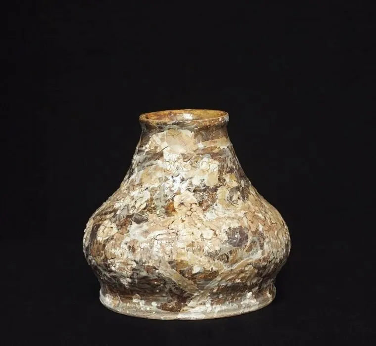 A squat marbled vase with gold and cream tones against black